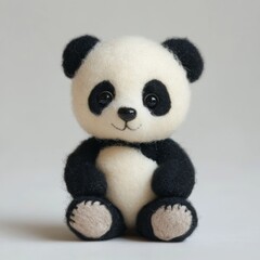 A small, handcrafted panda bear made from felt. The panda is sitting on a light gray background with its black and white fur, black eyes, and brown paw pads clearly visible.