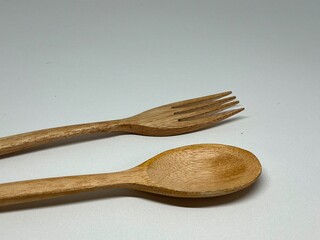 Two wooden utensils, a fork and a spoon, resting on a neutral background.