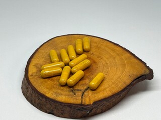 Yellow capsules arranged on a wooden slice, possibly dietary supplements or medication.