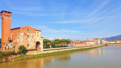Fototapeta premium View of the brown tower Guelph and the street of Pisa from the bridge of the Arno river. Panorama.