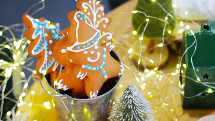 Festive Gingerbread Cookies with Christmas Lights. A cup of gingerbread cookies with a Christmas tree in the background. Close-up of beautifully decorated gingerbread cookies shaped like a Christmas