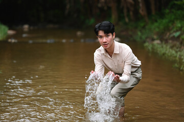 A young man playfully splashes water in a river, with focus and joy in his expression, embracing a...