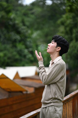 Fototapeta premium A young man breathes cold air as he looks into the distance amidst greenery, enjoying a quiet moment outdoors
