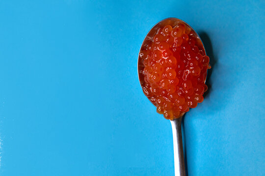 A tablespoon full of red caviar on a light blue background.