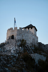 Old Town Fortress of Uzice in Serbia country. Ancient castle with Serbian tricolor flag on sunny evening. View from below from the gorge, sunset mood. Blue hour