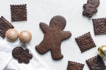 Overhead view of stamped molasses cookies and gold Christmas ornaments on a parchment lined baking tray, top view of embossed gingerbread cookies and gold Christmas baubles on a white background