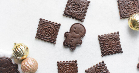 Overhead view of stamped molasses cookies and gold Christmas ornaments on a parchment lined baking tray, top view of embossed gingerbread cookies and gold Christmas baubles on a white background