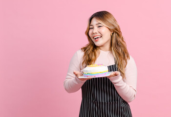 Photo cute happy fun young Asian beautiful female, woman smiling wearing aprons holding cake sweet dessert poses isolated plain pastel light over pink color wall background.