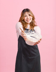 Photo cute happy funny young Asian beautiful female, woman smiling wearing aprons holding baking equipment makes homemade cake poses isolated plain pastel light over pink color wall background.