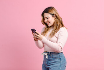 Photo cute happy fun young Asian beautiful female, woman smiling in light pink long-sleeve shirt and holding mobile phone poses isolated plain pastel light over pink color wall background.