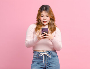 Photo cute happy fun young Asian beautiful female, woman smiling in light pink long-sleeve shirt and holding mobile phone poses isolated plain pastel light over pink color wall background.