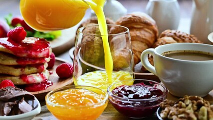 Filling glass with orange juice on table with breakfast