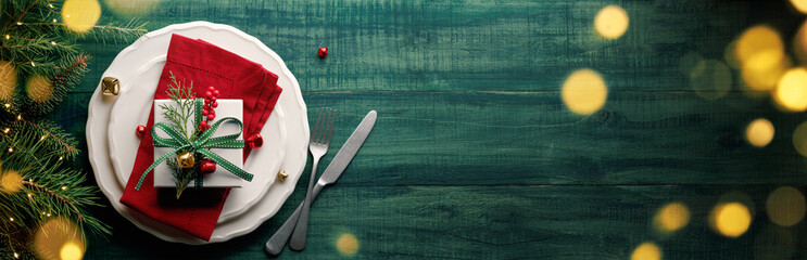 Christmas gift box on plate with cutlery and fir branches on wooden table.