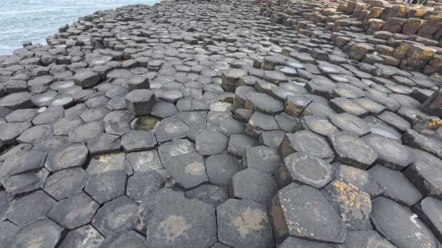 Forward moving shot over basalt columns along the Atlantic shore at Giant Causeway in Northern Ireland with the camera facing downward capturing the unique formations