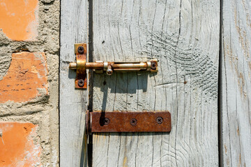 Old wooden door with a rusty metal lock on the background of a worn brick wall