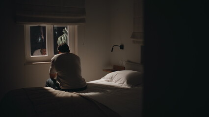 Silhouette sad man sitting bed home looking window feeling lonely. Guy insomnia