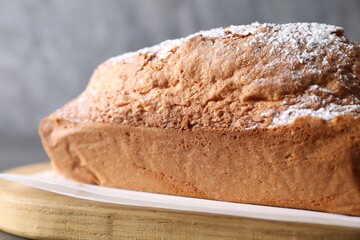 Tasty sponge cake with powdered sugar on table, closeup