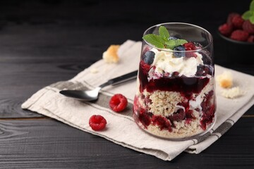 Tasty trifle dessert. Berries, sponge cake and whipped cream in glass on black wooden table, space for text