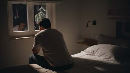Fototapeta premium Depressed guy sitting bedding by window at night feeling anxious. Pensive man 