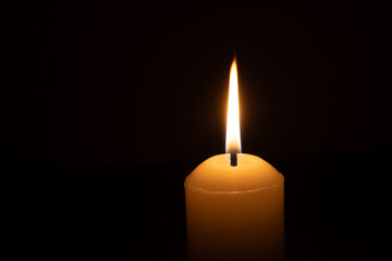 A single burning candle flame or light glowing on a big white candle isolated on red or dark background on table in church for Christmas, funeral or memorial service