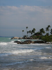 The beach is a breathtaking sight, with soft, powdery white sand stretching as far as the eye can see. The water is a mesmerizing shade of clear blue, sparkling under the bright sun, inviting you to