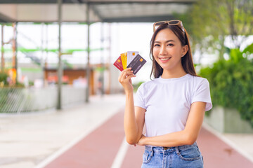 Portrait of Happy Asian woman holding credit card standing in shopping mall. Attractive girl enjoy and fun urban lifestyle shopping at department store on holiday vacation. Cashless payment concept.