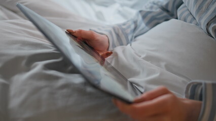 Girl hands holding tablet in morning bed closeup. Unknown woman watching seminar