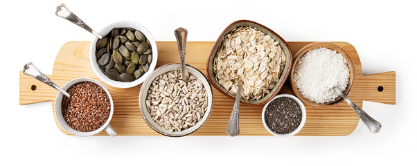 Variety of seeds and ingredients for a healthy diet: pumpkin, chia, oats, sunflower and dehydrated coconut flakes on cutting board isolated on white background. Top view, flat lay.