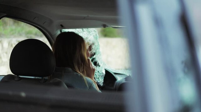 Woman Sit Inside Car With Broken Windshield, Making Phone Call for Help After Experiencing an Accident. Damaged Glass Indicates Recent Collision and Distress