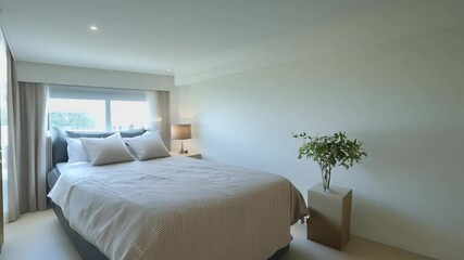 Camera slowly does a 360-degree video in a minimalist bedroom with ambient light, white walls, a king-sized bed, and a plant - Powered by Adobe