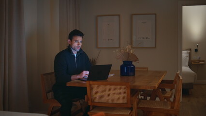 Late worker video calling by laptop in evening home office. Freelancer talking