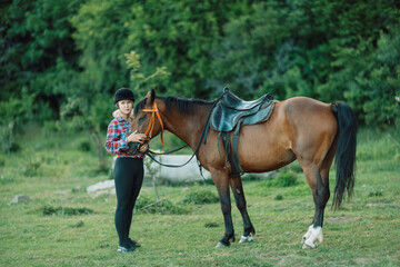Happy blonde with horse in forest. Woman and a horse walking through the field during the day. Dressed in a plaid shirt and black leggings.