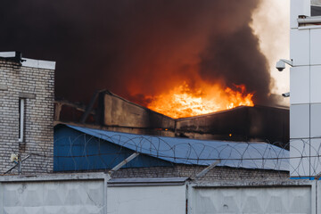 Massive large blaze fire in the city, blazing warehouse factory, storage building is burning, firefighters team putting out the fire, firemen on duty, extinguish the fire, arson, burning house damage