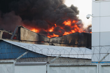 Massive large blaze fire in the city, blazing warehouse factory, storage building is burning, firefighters team putting out the fire, firemen on duty, extinguish the fire, arson, burning house damage