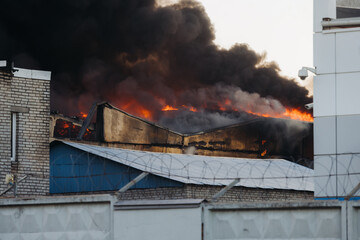 Massive large blaze fire in the city, blazing warehouse factory, storage building is burning, firefighters team putting out the fire, firemen on duty, extinguish the fire, arson, burning house damage