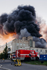 Fototapeta premium Massive large blaze fire in the city, blazing warehouse factory, storage building is burning, firefighters team putting out the fire, firemen on duty, extinguish the fire, arson, burning house damage