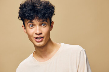 Portrait of a surprised young man with curly hair He is looking at the camera, demonstrating an expression of curiosity or amazement against a neutral beige background