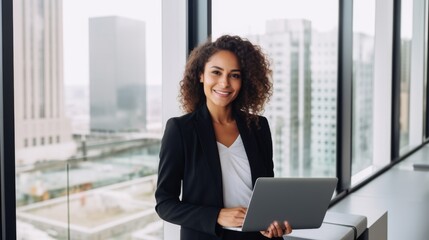 Fototapeta premium A confident businesswoman smiles while holding a laptop in a high-rise office, embodying success and professionalism against a cityscape backdrop.