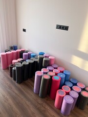 Colorful foam massage rollers neatly arranged in rows on a wooden floor against a white wall, ready for fitness or physiotherapy use.