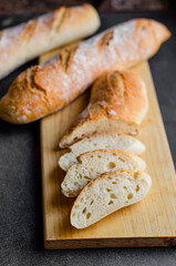 A close-up photo of fresh, golden-brown baguette slices arranged on a rustic wooden cutting board. The bread has a crusty exterior and soft, airy interior, making it ideal for food blogs, bakery promo
