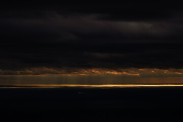 Dark clouds gather over the ocean as the sun sets, casting a golden glow across the water and creating a dramatic sky view. Dramatic twilight clouds illuminate the horizon above the ocean at sunset.