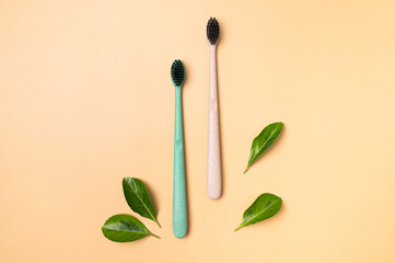 Multicolored eco-friendly bamboo toothbrushes with green leaves on beige background. Natural accessories for oral hygiene, no plastic. Dental health concept top view flat lay
