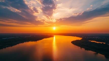 Obraz premium An aerial view of a river winding through a landscape at sunset. The sun is setting in the distance, casting a golden glow on the water.