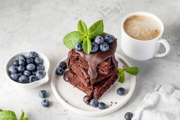 Stack of chocolate brownies with chocolate glaze, fresh berries and mint leaves on white plate on white kitchen background, text space