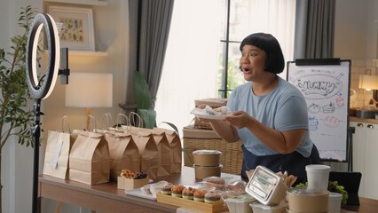 Woman presenting homemade baked goods online, surrounded by bakery items on a table, showcasing her culinary skills in a cozy home setting.