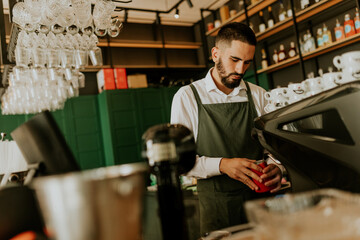 A barista skillfully prepares beverages in a stylish cafe, surrounded by an elegant display of glassware and rich colors