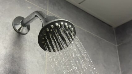 Shower head covered with scale, dirt with a cascading stream of water in the shower stall. Close-up.