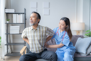 Young female nurse wearing blue scrubs is examining the lower back of an elderly male patient experiencing discomfort