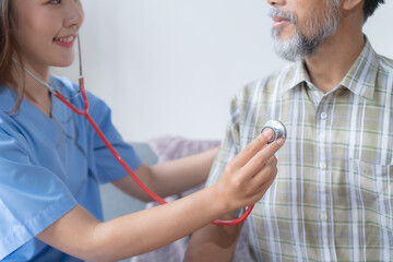 Female doctor is listening to the heartbeat of a senior man with a stethoscope, providing in-home healthcare and monitoring his vital signs