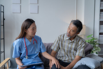 Obraz premium Young female doctor is comforting her senior patient during a home visit while holding a tablet and listening to his concerns